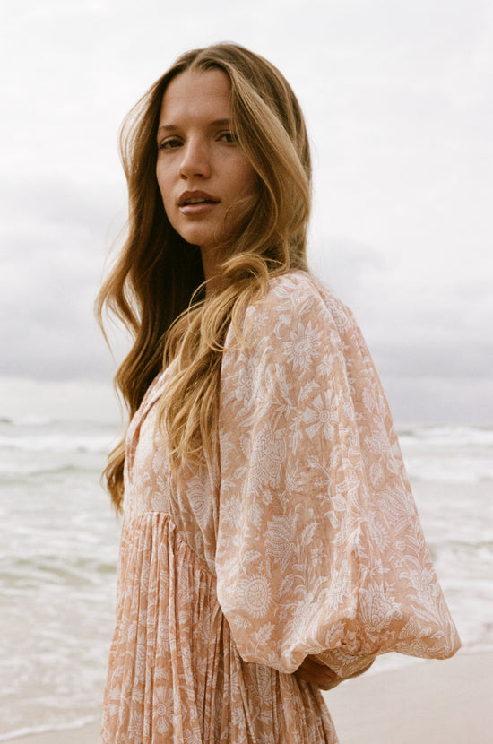 Daughters of India Kyra Maxi Dress in Apricot Blush — side profile at ocean, billowed sleeve and floral print detail