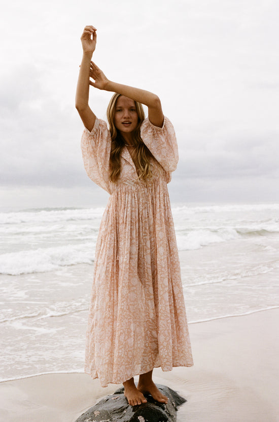 Daughters of India Kyra Maxi Dress in Apricot Blush — on rock at ocean edge arm raised, hand screen print cotton maxi