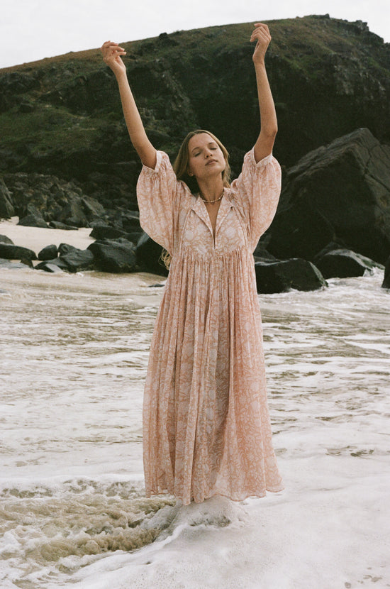 Daughters of India Kyra Maxi Dress in Apricot Blush — arms raised in waves, flowing hand screen print cotton maxi