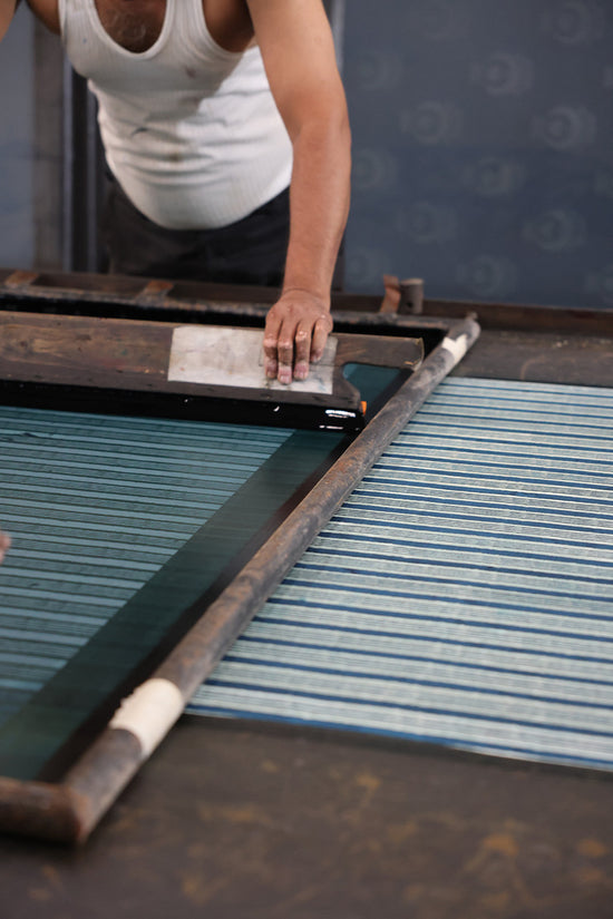 Indian artisan working with a screen printing frame on the Spearmint striped fabric for Daughters of India, demonstrating traditional handcraft techniques