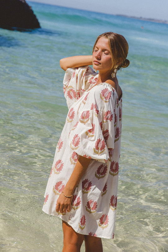 Ria Mini Dress Strawberry Cream — beach lifestyle shot, model wearing strawberry cream floral hand block print cotton mini dress, short hemline with relaxed fit, artisan Jaipur India | Daughters of India