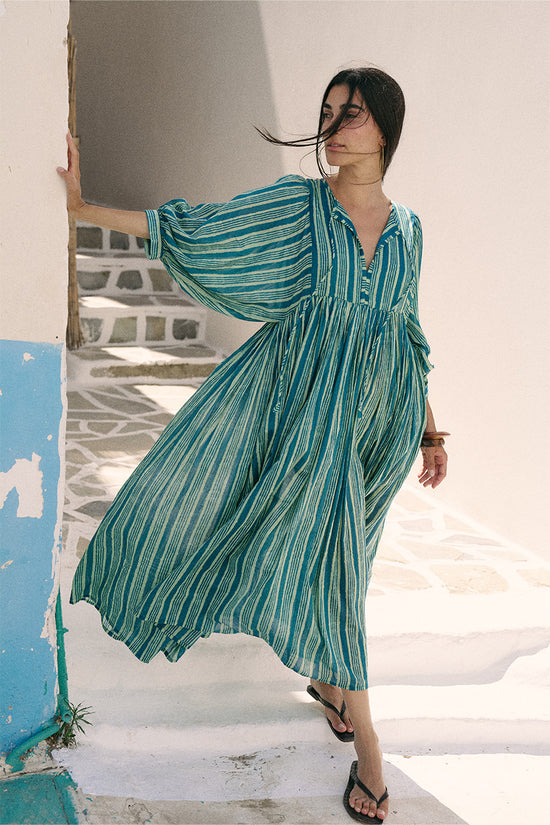 Woman standing on a white staircase wearing the Daughters of India Kyra Maxi Dress in Spearmint with the fabric billowing in the breeze, Greek island backdrop