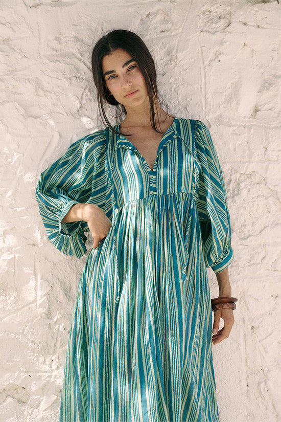 Woman posing against a white textured wall wearing the Daughters of India Kyra Maxi Dress in Spearmint, showing the button neckline and relaxed maxi silhouette
