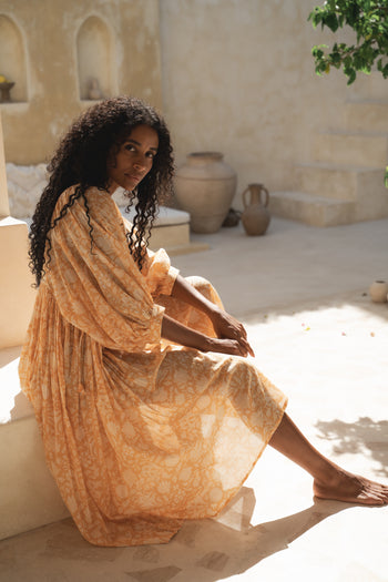 Daughters of India Kyra Midi Dress in Tangerine — seated in sunlit courtyard, hand screen print cotton